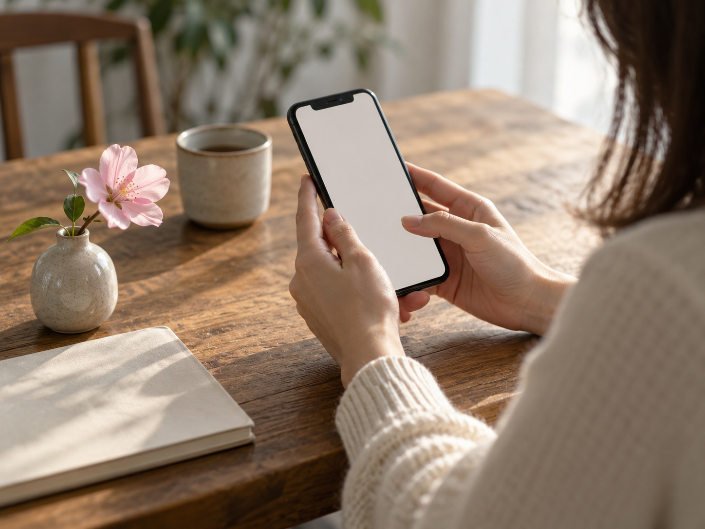 Hands holding a phone with a blossom nearby